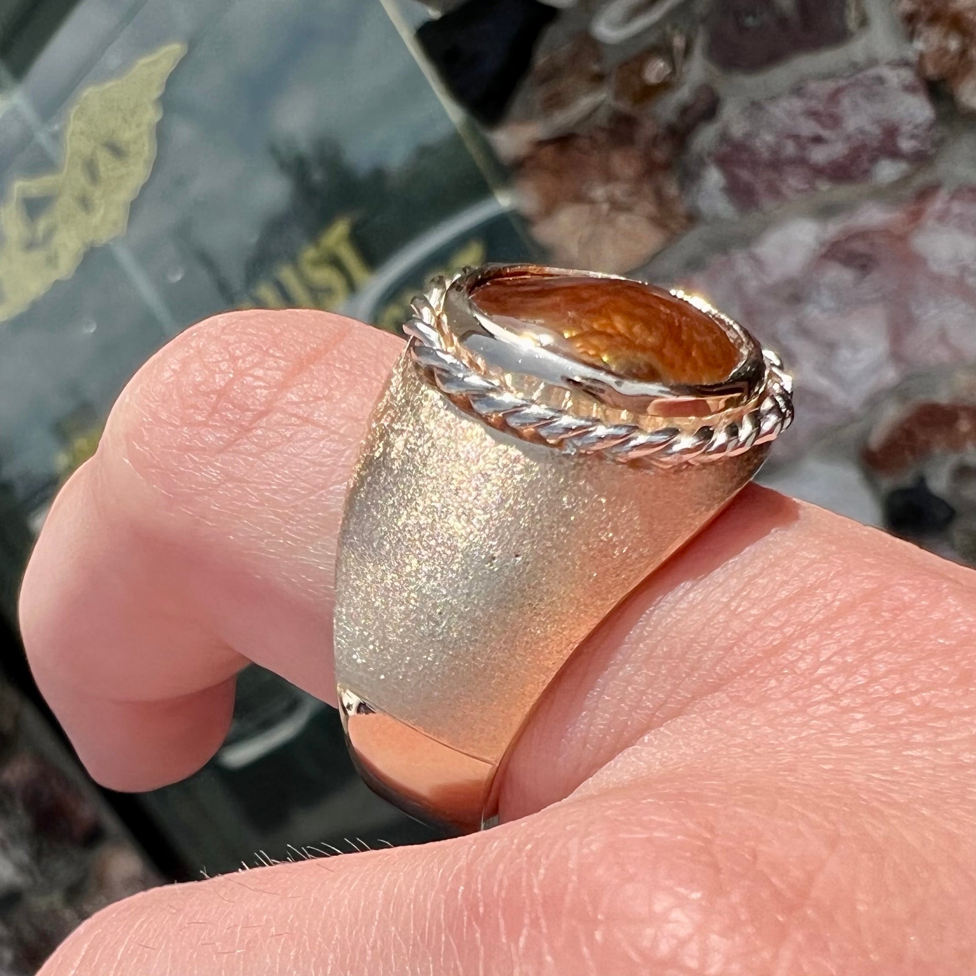 A men's matte finish textured gold fire agate ring.  There is a gold rope bezel around the oval cabochon cut stone.
