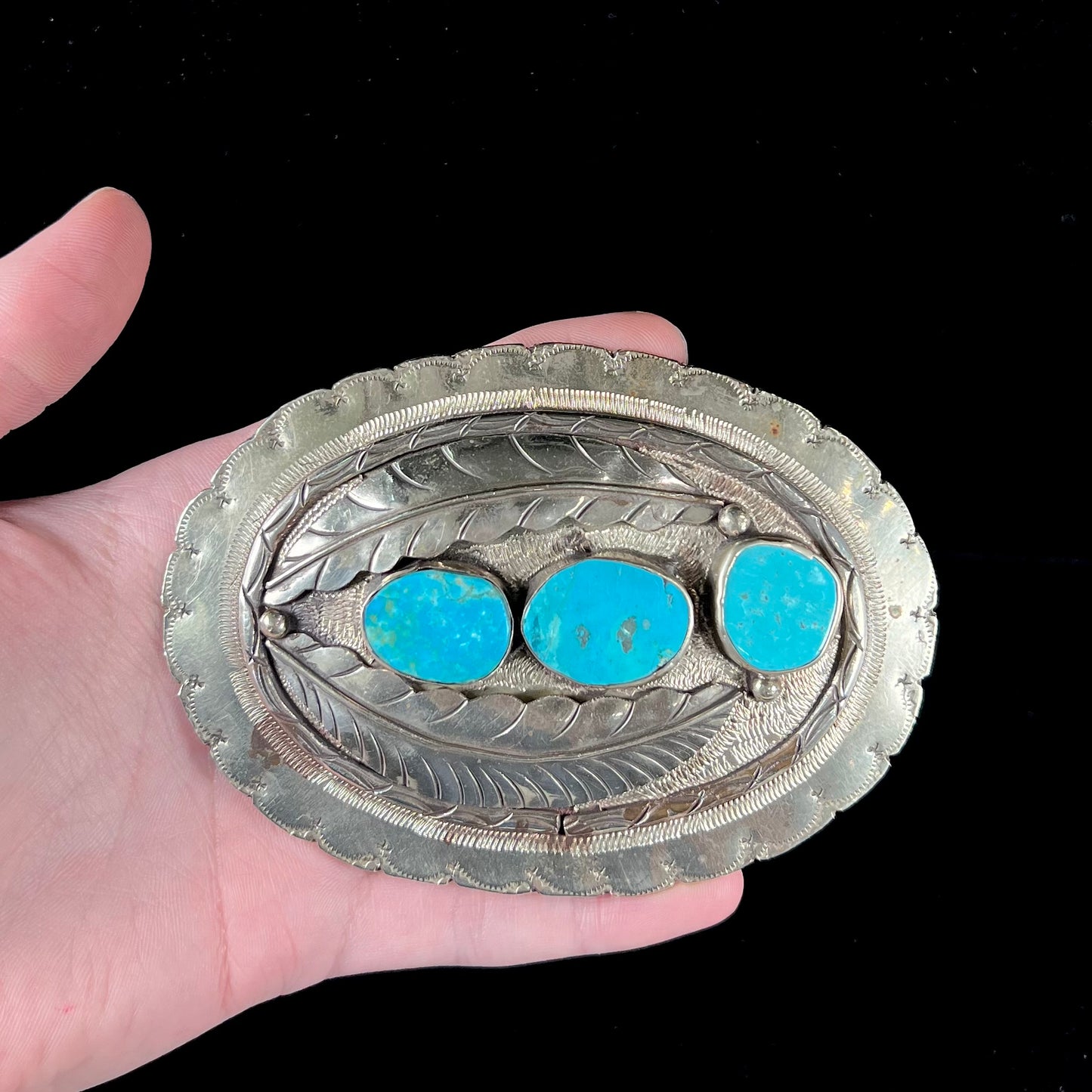 A vintage men's Navajo-made three stone turquoise belt buckle.  The belt buckle is base metal and has a feather design.