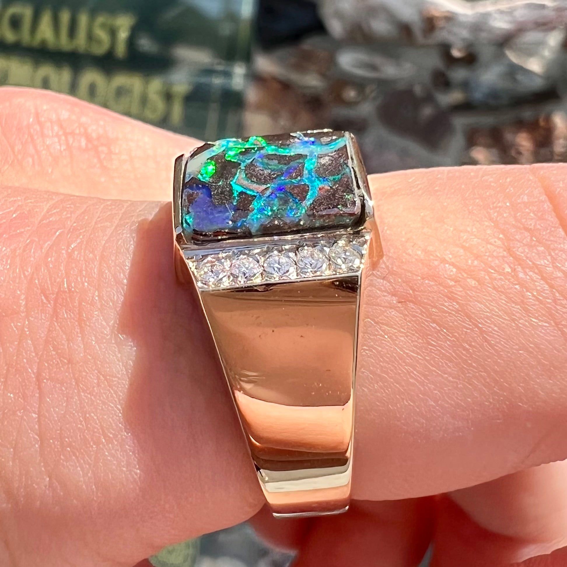 A men's gold boulder opal and diamond ring.  The opal shows blue and green colors.