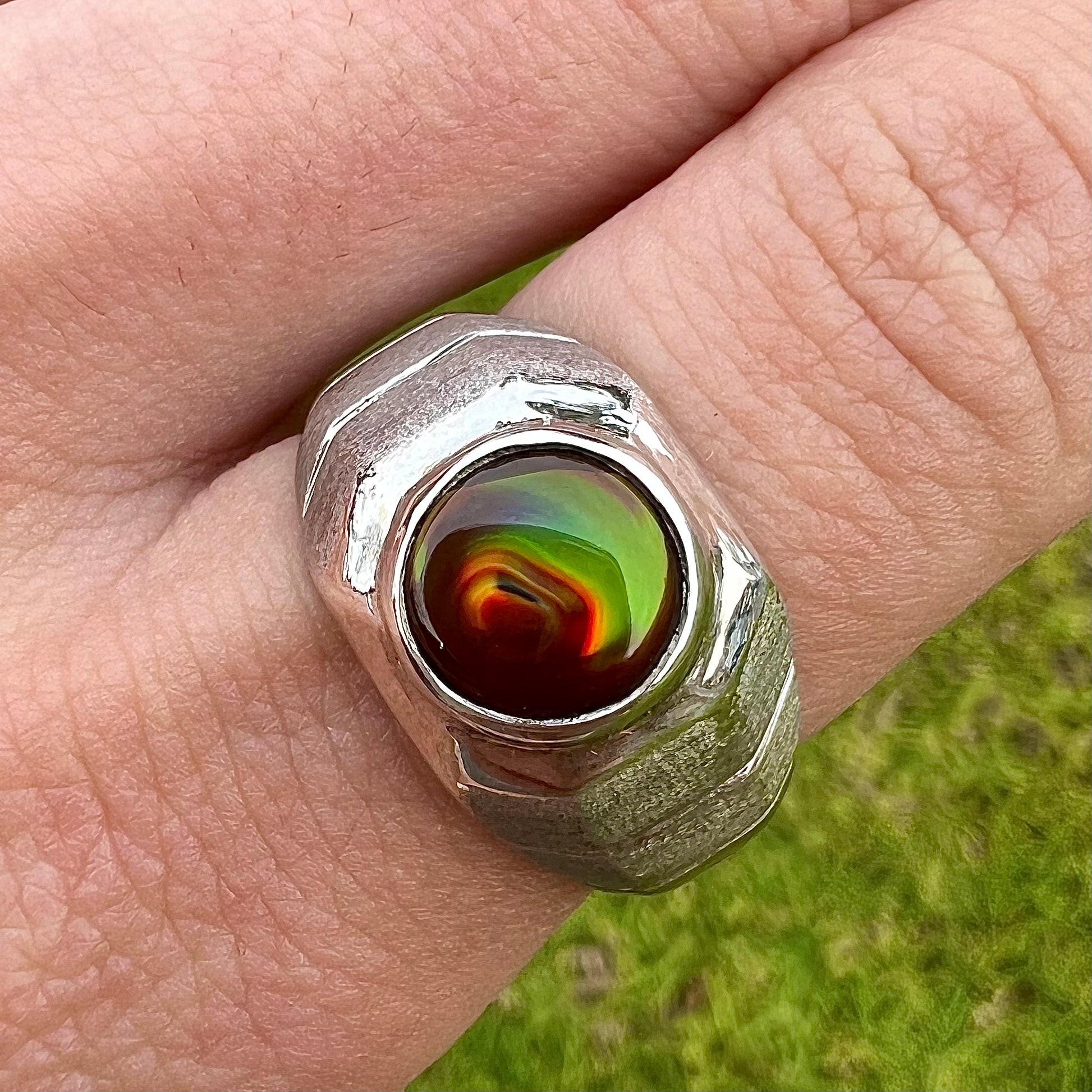 A round cabochon cut red and green fire agate set in a brushed metal white gold men's ring.