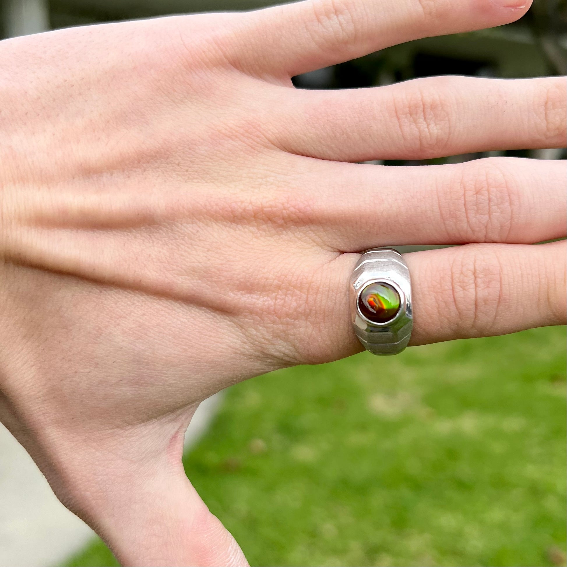 A round cabochon cut red and green fire agate set in a brushed metal white gold men's ring.