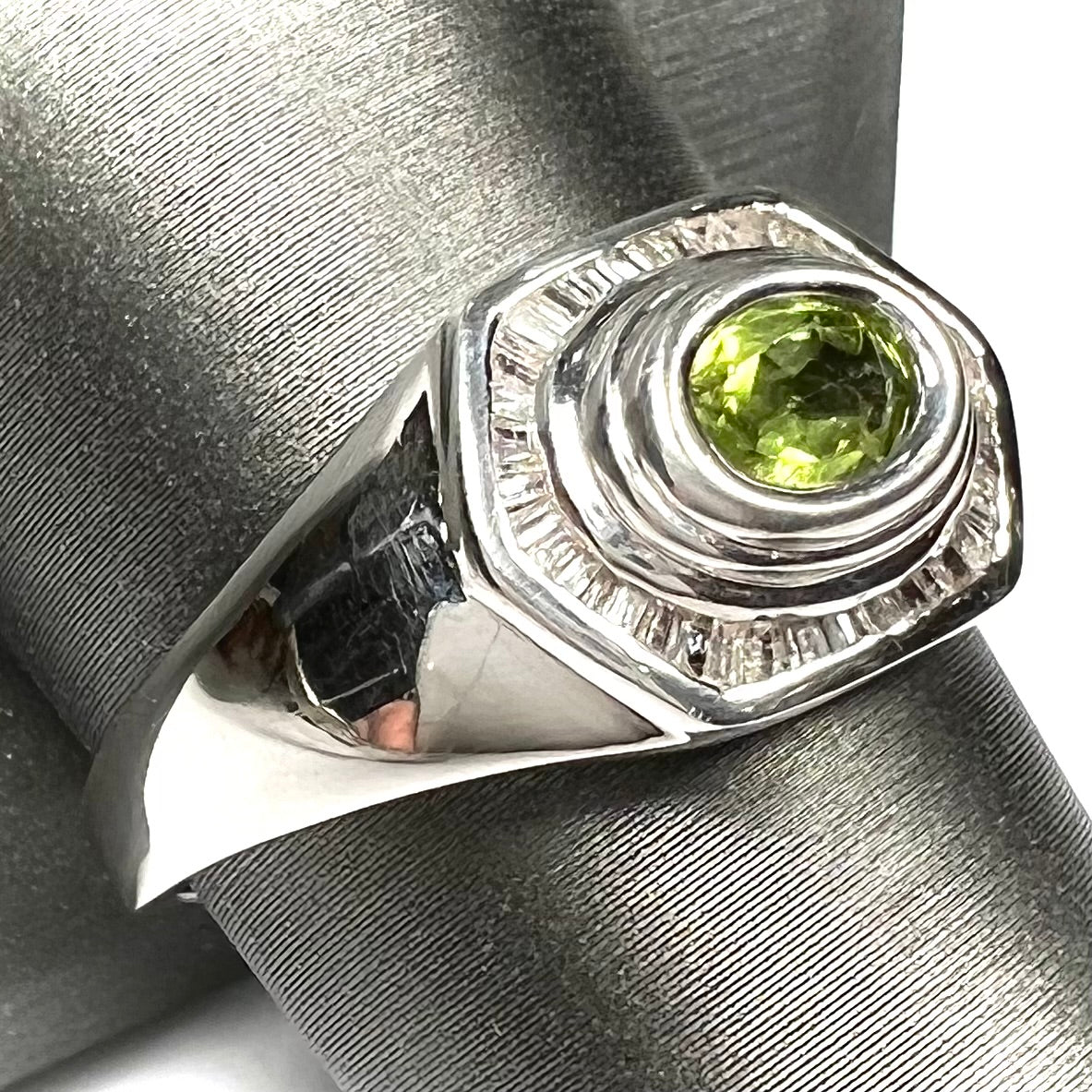 A sterling silver men's ring set with green peridot surrounded by baguette cut diamonds.