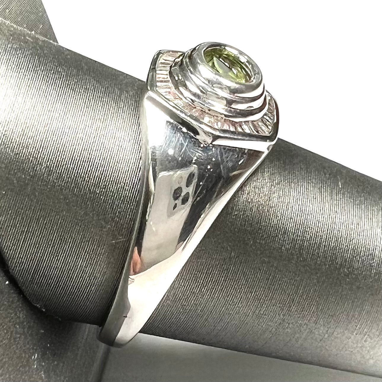 A sterling silver men's ring set with green peridot surrounded by baguette cut diamonds.