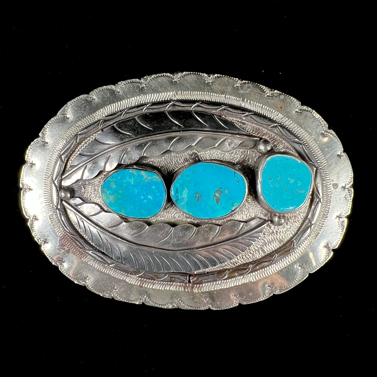 A vintage men's Navajo-made three stone turquoise belt buckle.  The belt buckle is base metal and has a feather design.