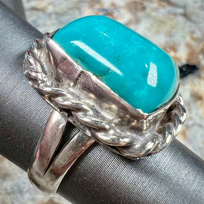 A sterling silver turquoise split shank ring.  There is a handmade silver rope around the turquoise.