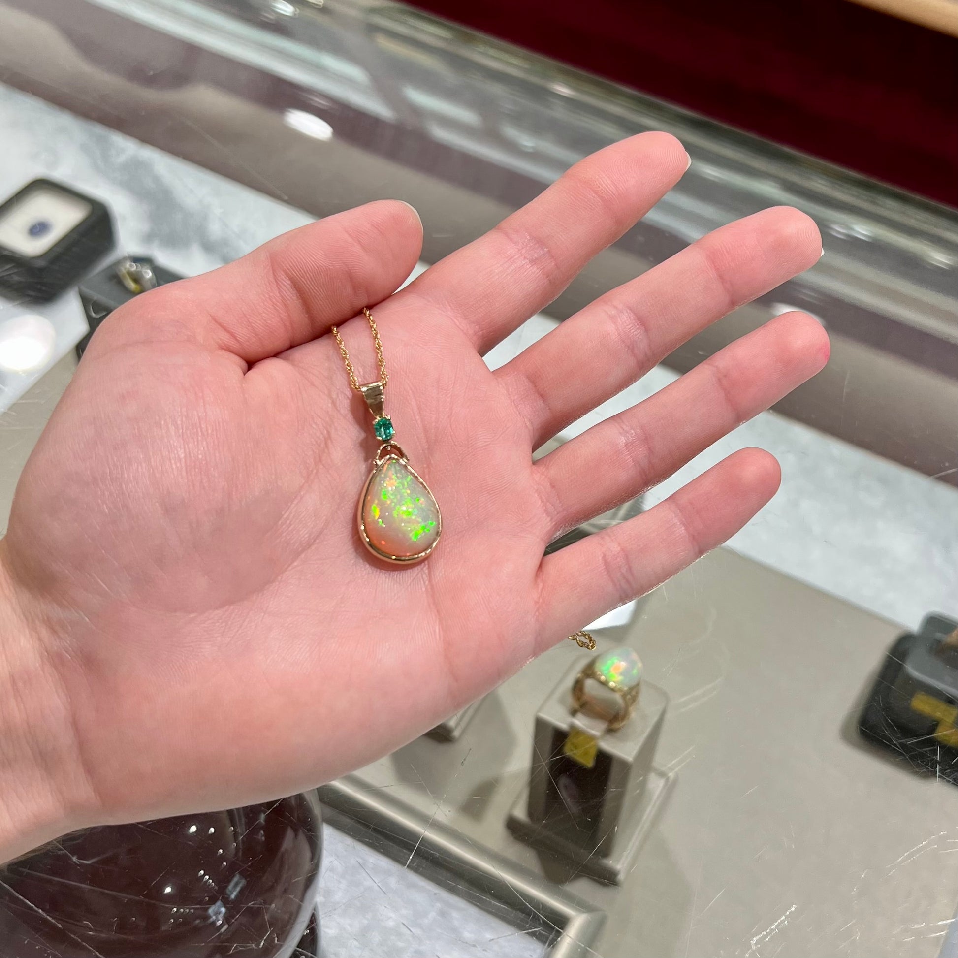 A yellow gold bezel set Ethiopian fire opal drop pendant.  There is an emerald set in the bail.