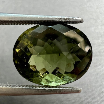 A loose faceted checkerboard oval cut moldavite stone.