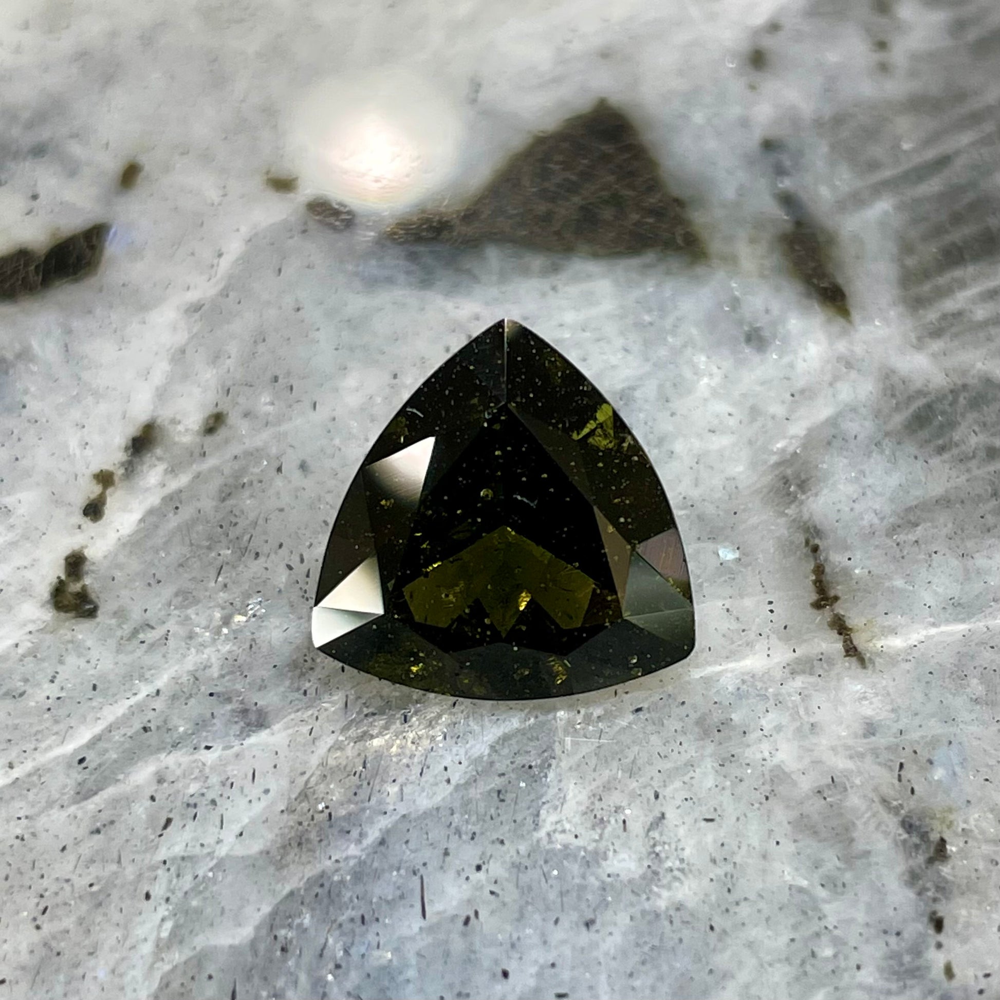 A faceted trillion cut moldavite gemstone that weighs 3.98 carats.  The stone is a dark green color.