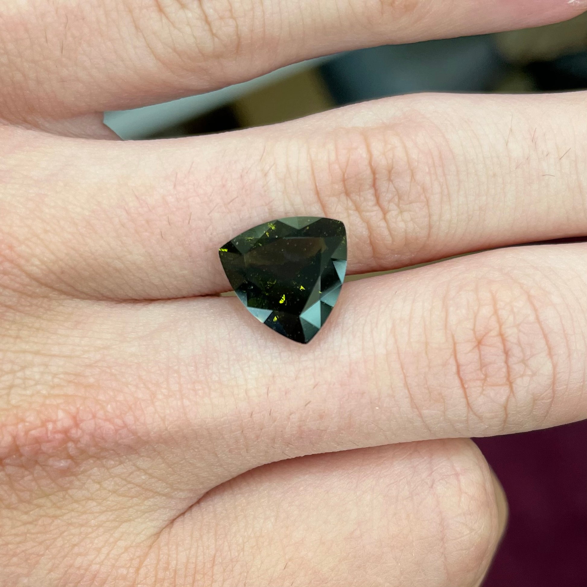 A faceted trillion cut moldavite gemstone that weighs 3.98 carats.  The stone is a dark green color.