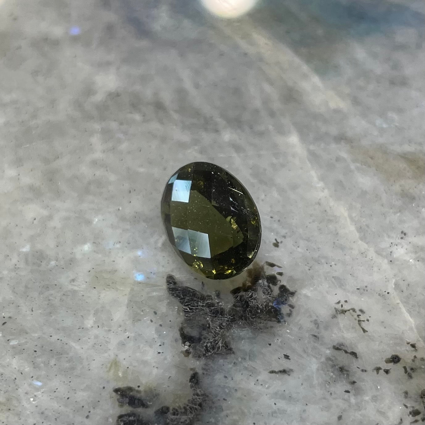 A loose, faceted oval cut moldavite gemstone.