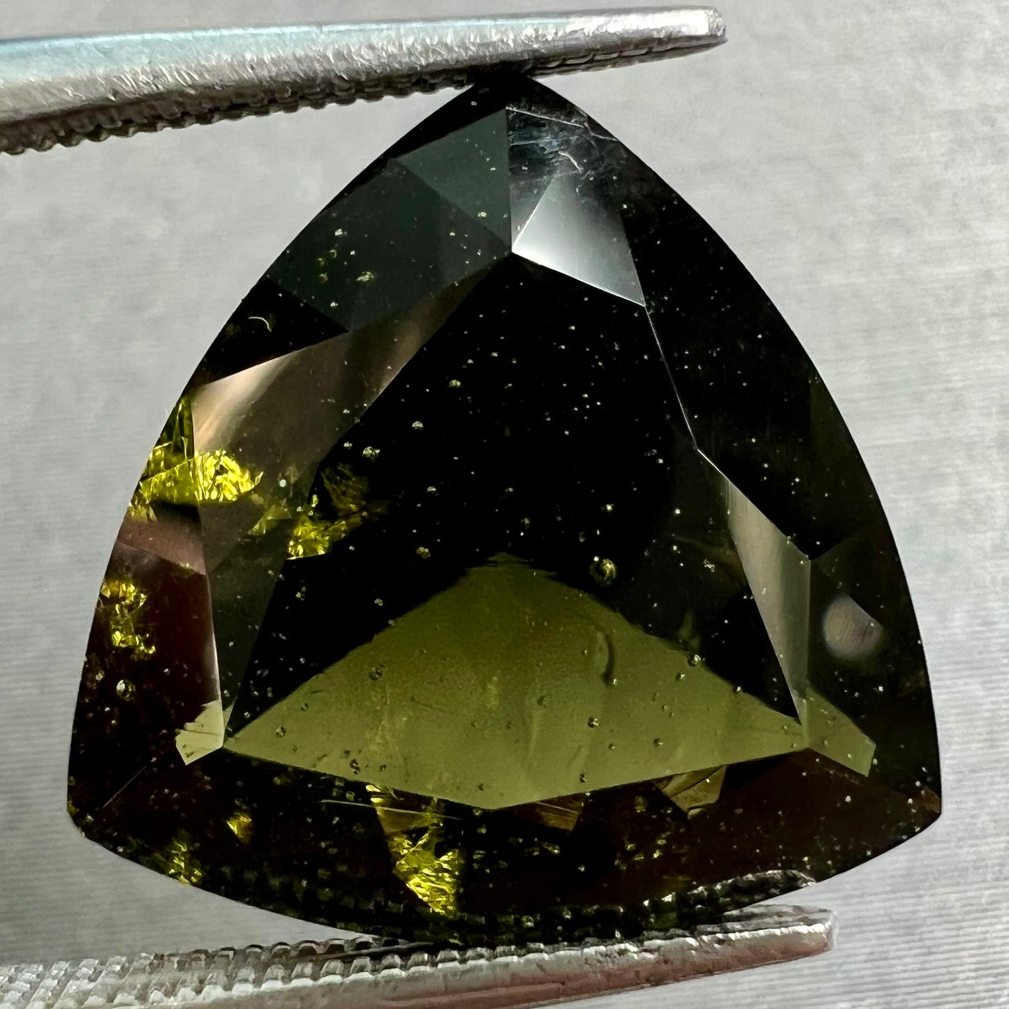 A faceted trillion cut moldavite gemstone that weighs 3.98 carats.  The stone is a dark green color.