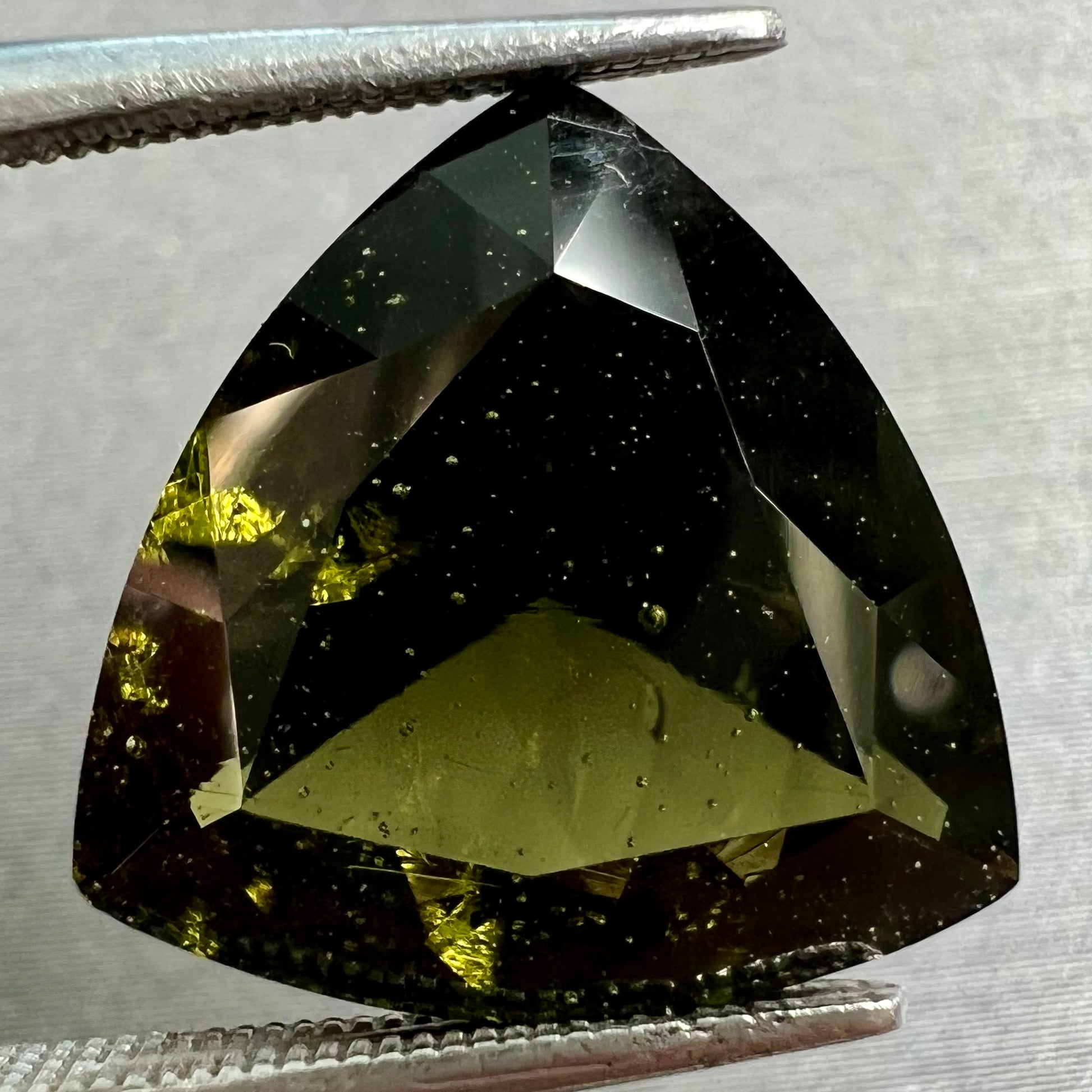 A faceted trillion cut moldavite gemstone that weighs 3.98 carats.  The stone is a dark green color.
