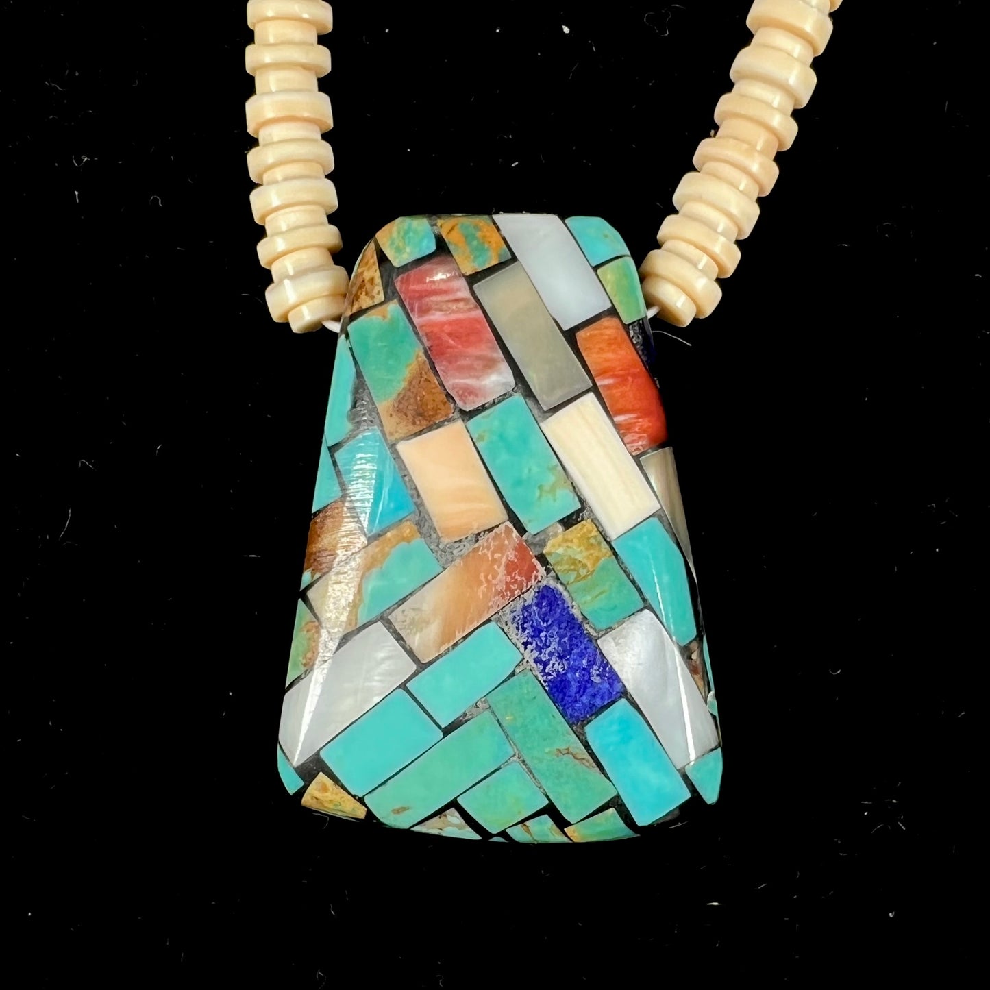 A three dimensional mosaic stone inlay pendant set with turquoise, lapis lazuli, coral, and mother of pearl on a puka shell necklace.