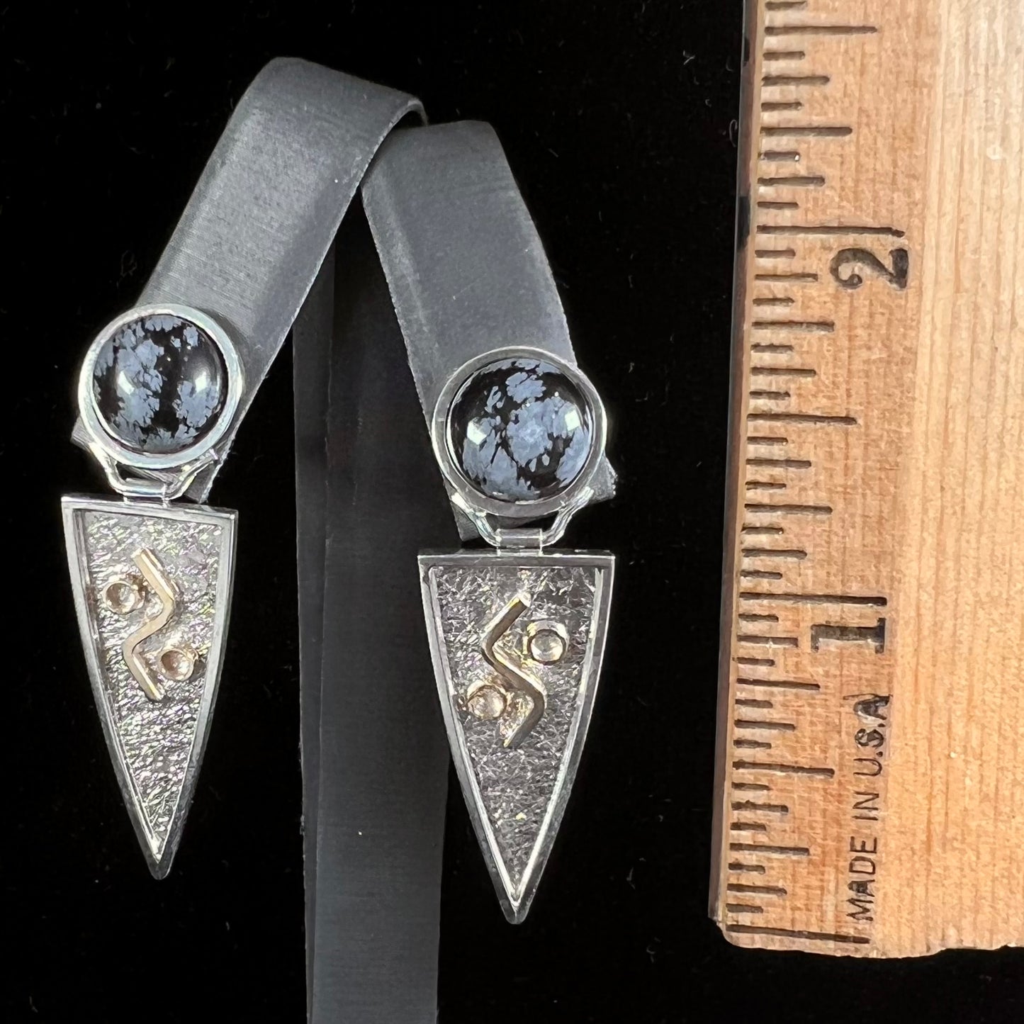 A pair of two-tone silver and gold snowflake obsidian earrings handmade by Zuni artist, Myron Panteah.