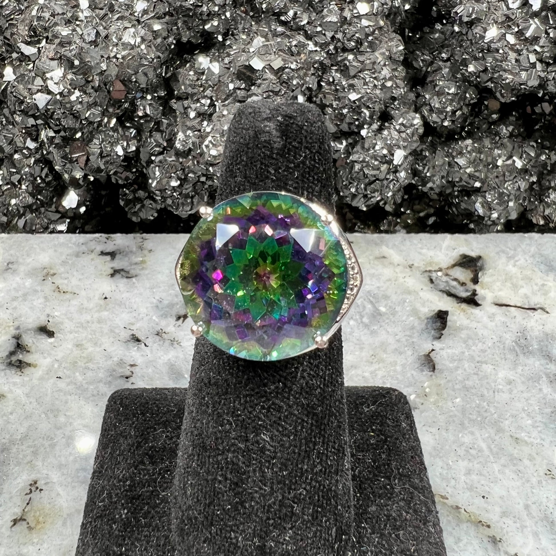 A large, round cut pink and green mystic topaz set in a sterling silver ring with white topaz accent stones.
