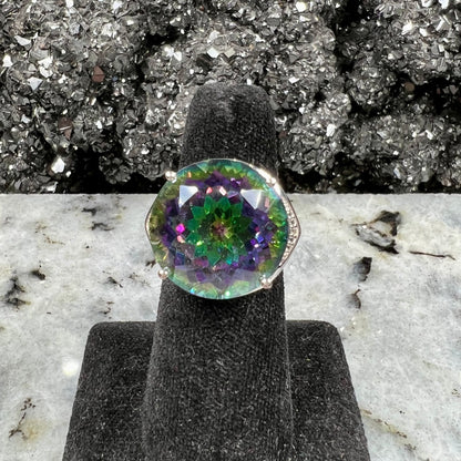A large, round cut pink and green mystic topaz set in a sterling silver ring with white topaz accent stones.