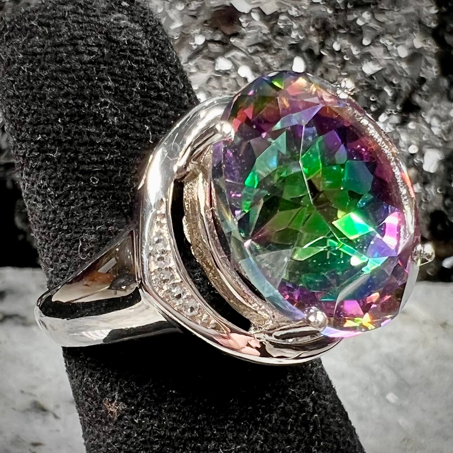 A large, round cut pink and green mystic topaz set in a sterling silver ring with white topaz accent stones.
