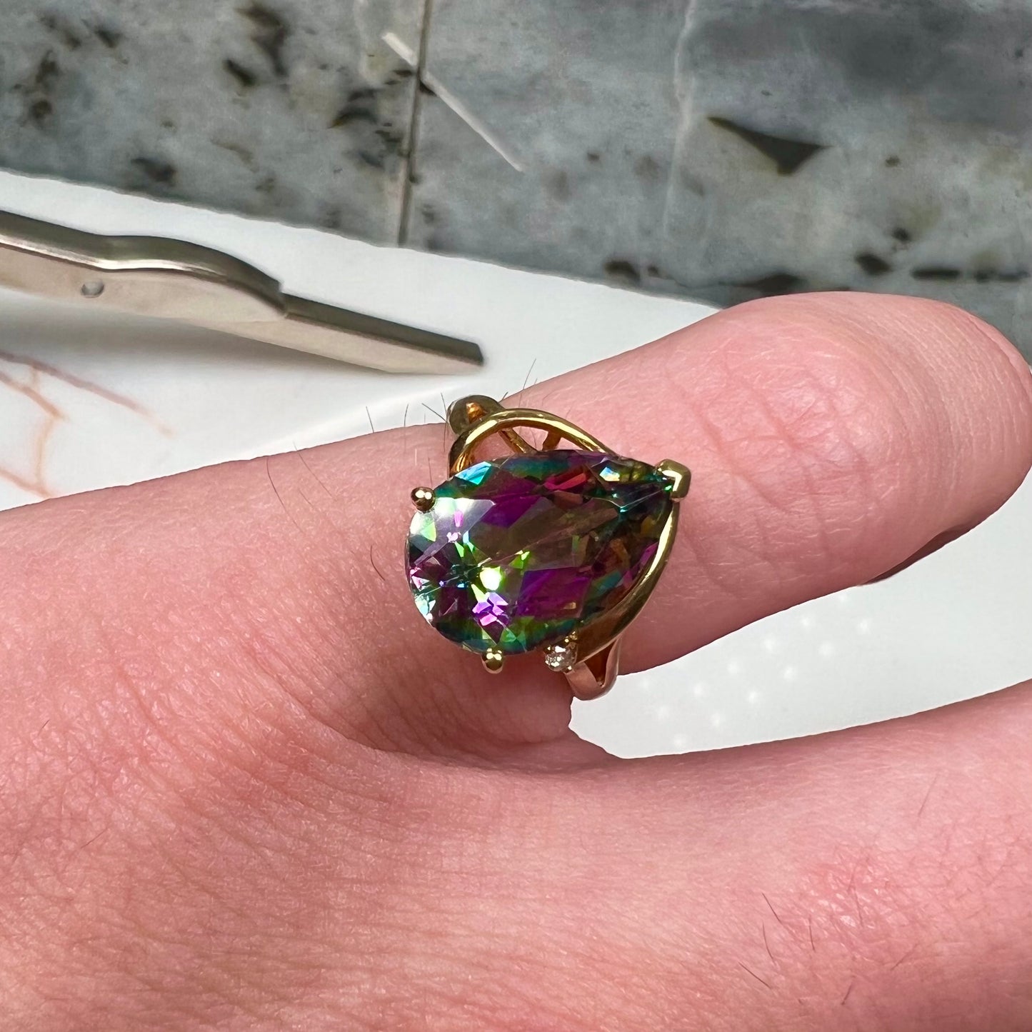 Pear shape green and pink mystic topaz set in a yellow gold ring with a single round diamond.