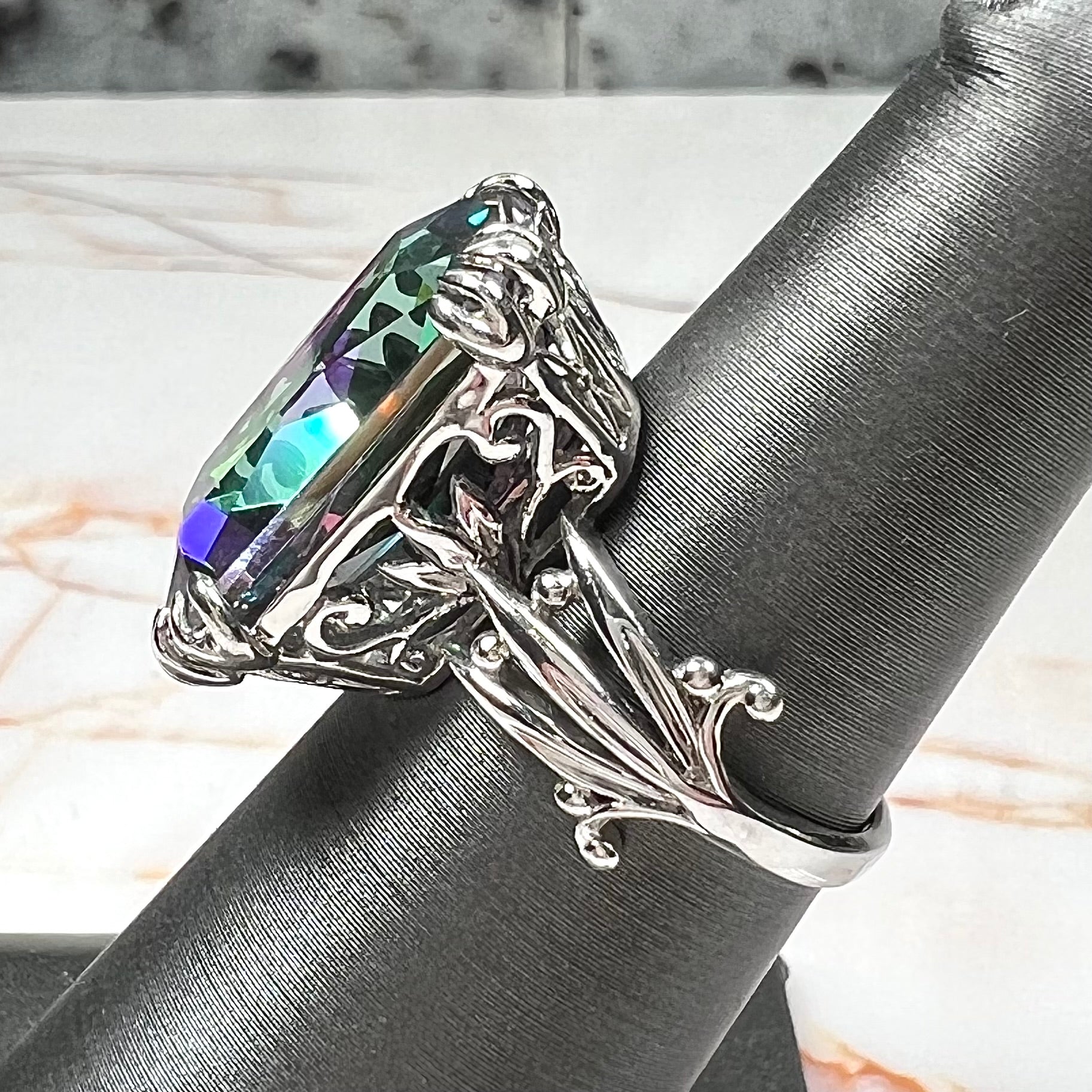 Emerald cut mystic topaz prong set in a decorative sterling silver ring.