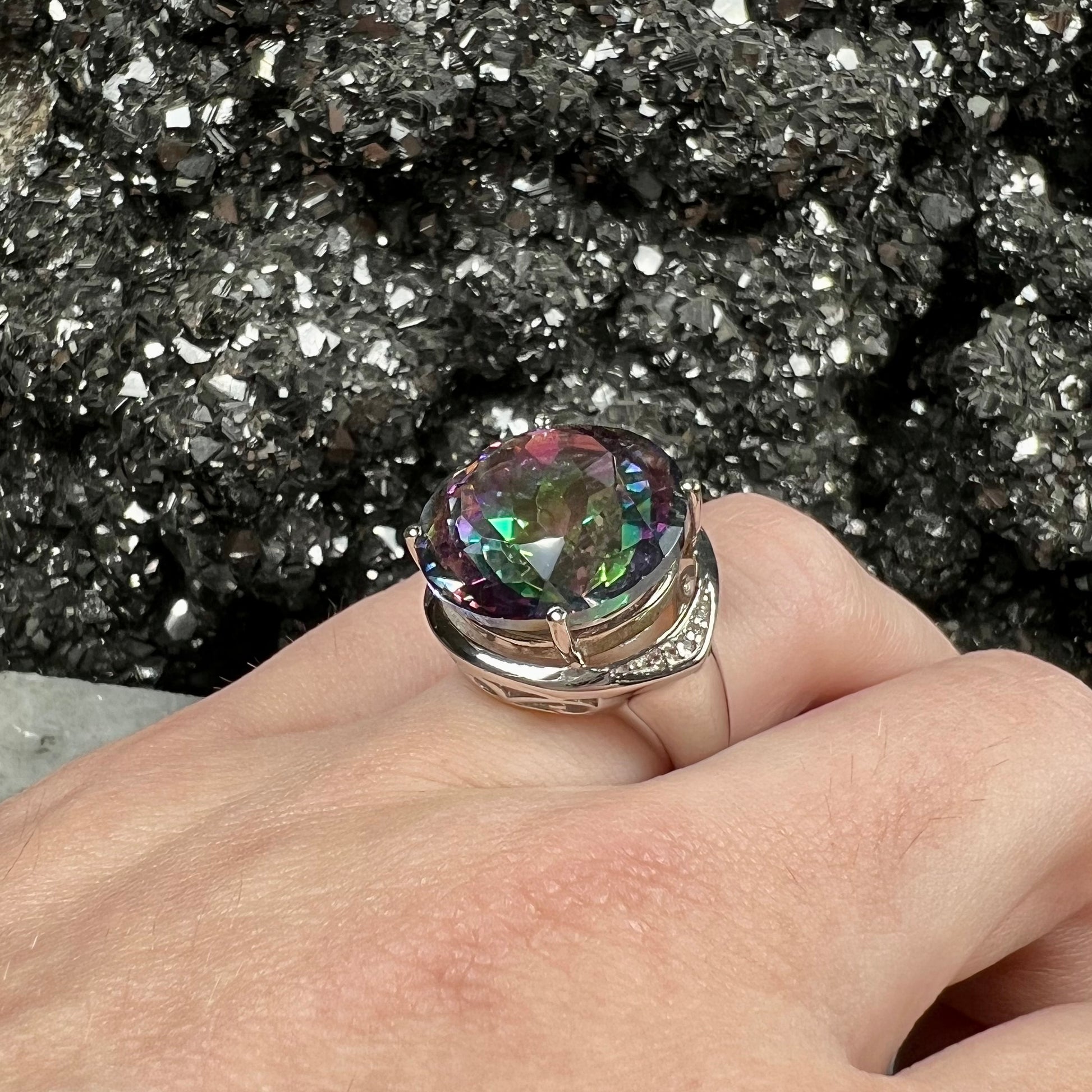 A large, round cut pink and green mystic topaz set in a sterling silver ring with white topaz accent stones.