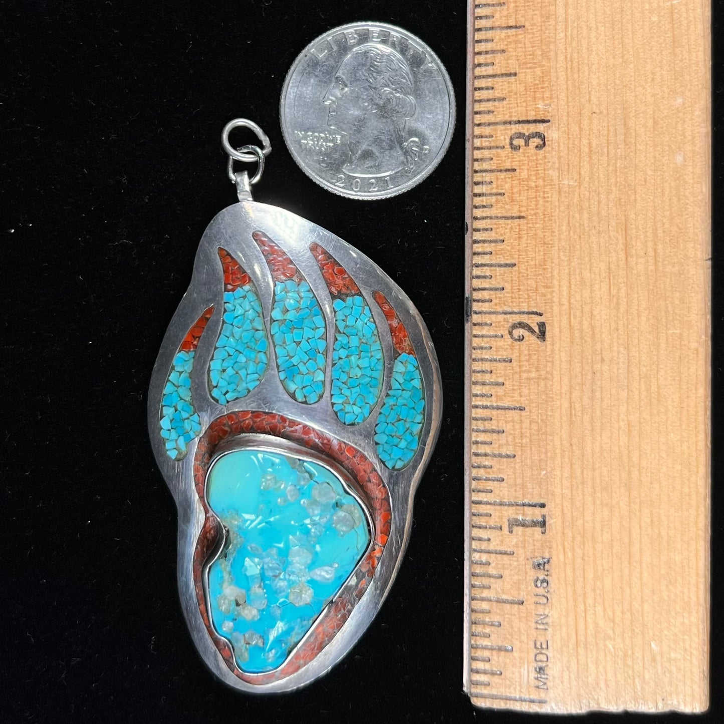 A sterling silver bear paw pendant set with Sleeping Beauty turquoise, crushed turquoise, and crushed coral.