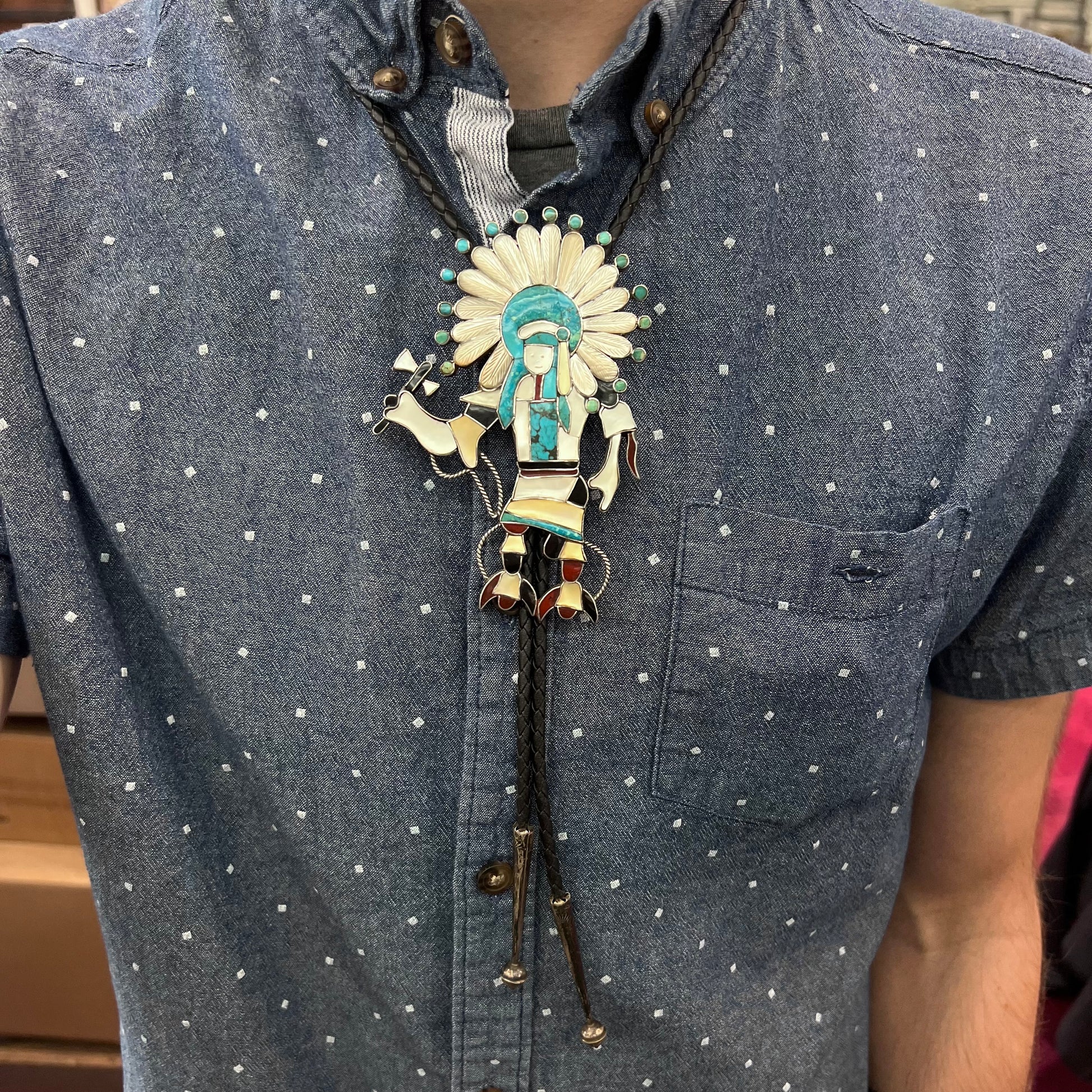 A Zuni Indian-made bolo tie featuring the motif of a kachina, inlaid with natural turquoise, mother of pearl, jet, and jasper stones.
