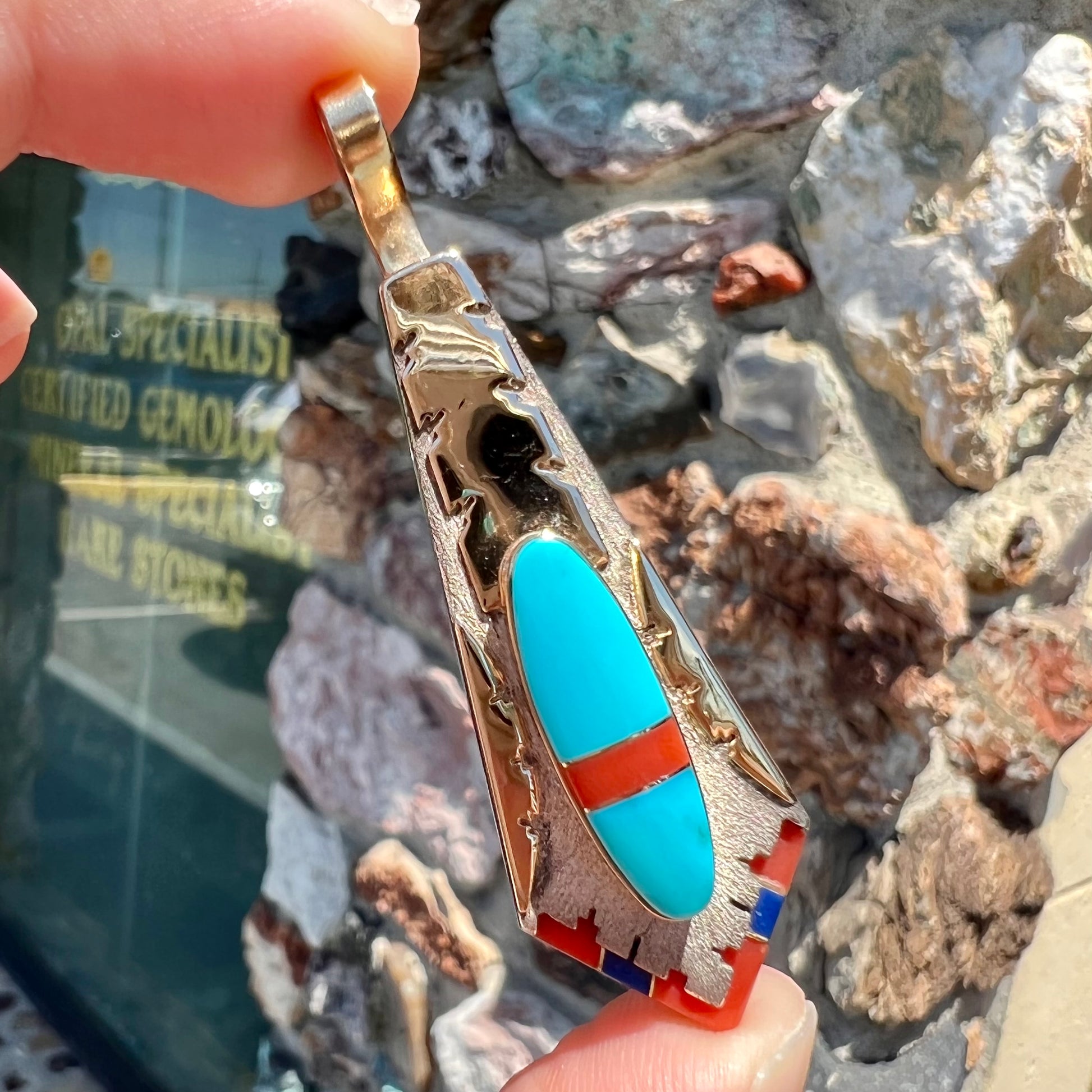 A yellow gold and sterling silver pendant inlaid with turquoise, coral, and lapis lazuli stones.  The piece is made by an unknown Native American artist and signed with the initials "LY".