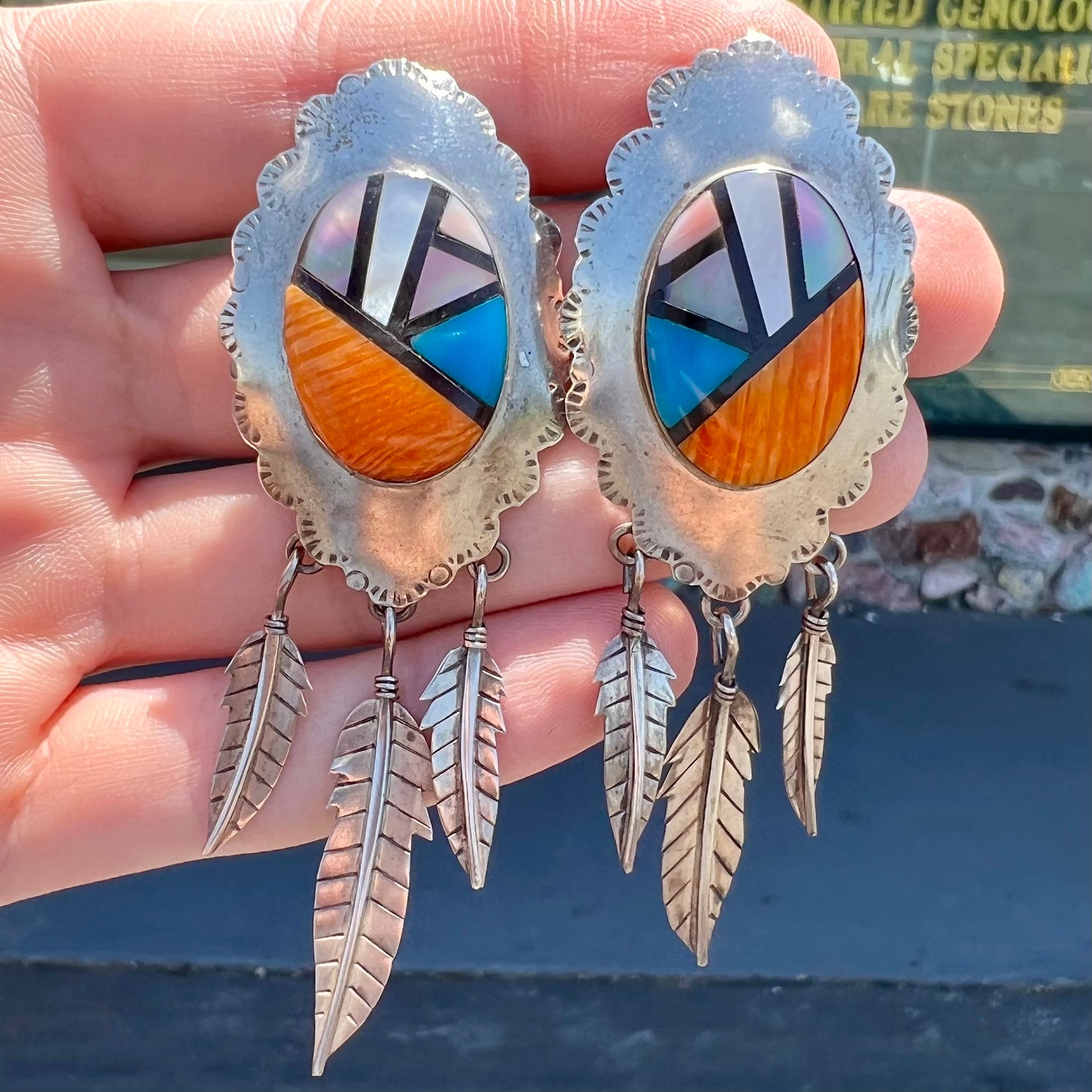 A pair of Native American style feather dangle earrings inlaid with mother of pearl shell and turquoise.