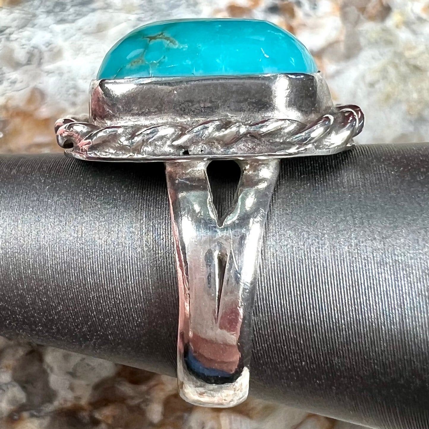 A sterling silver turquoise split shank ring.  There is a handmade silver rope around the turquoise.