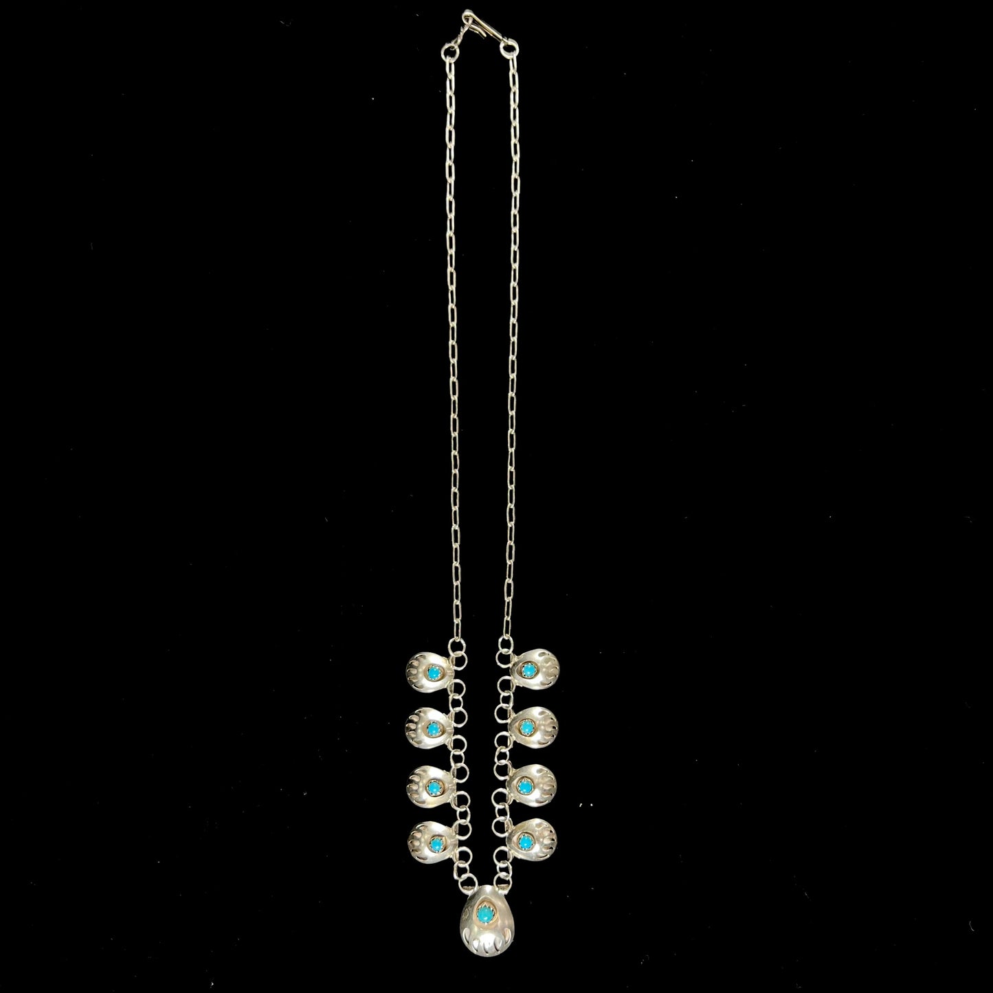 A silver turquoise necklace handmade with nine silver bear paws set with round turquoise stones.
