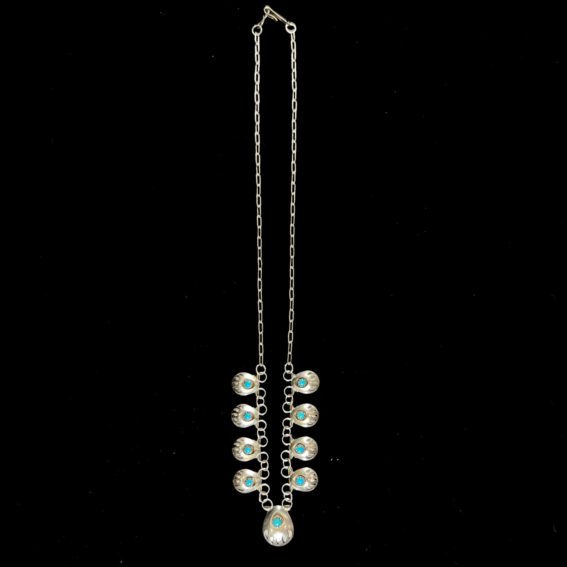A silver turquoise necklace handmade with nine silver bear paws set with round turquoise stones.