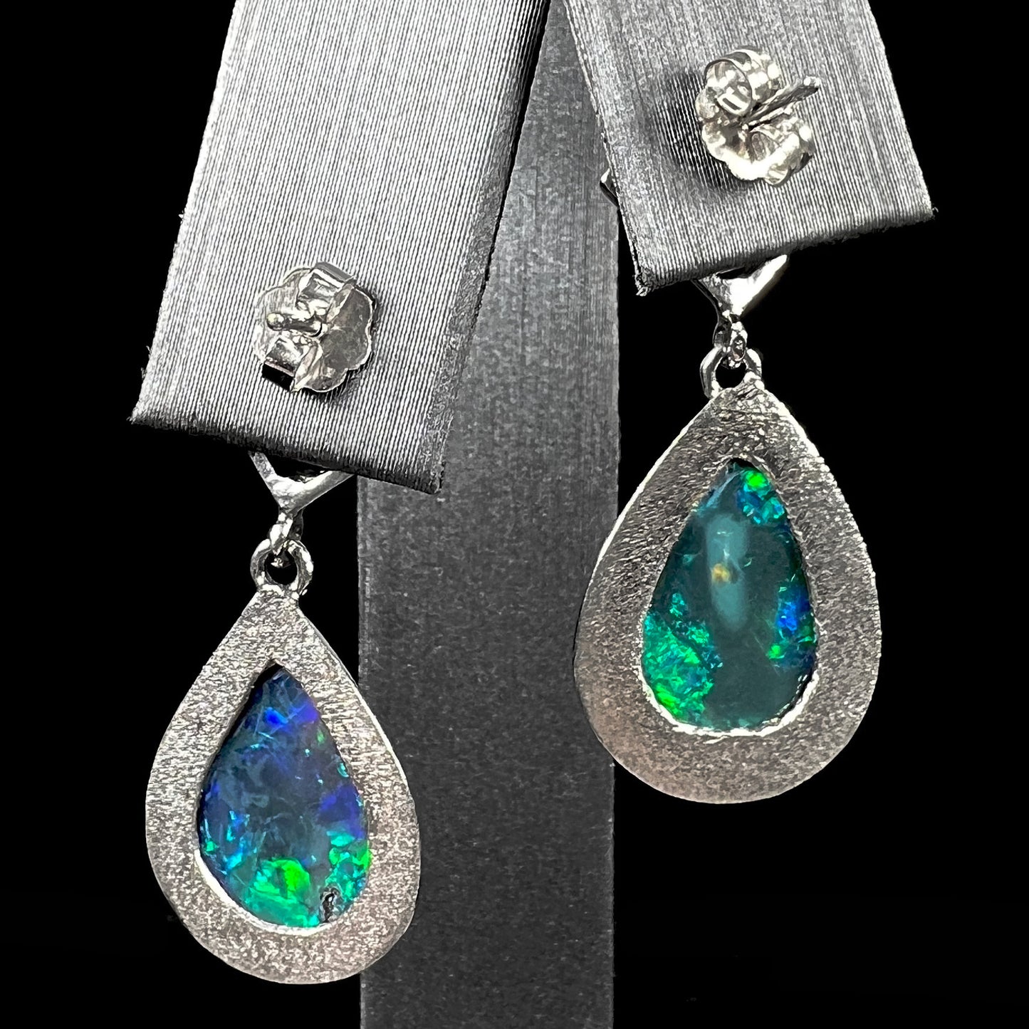 Black crystal opal dangle earrings with blue body color and green play of color set with princess cut diamonds in platinum.