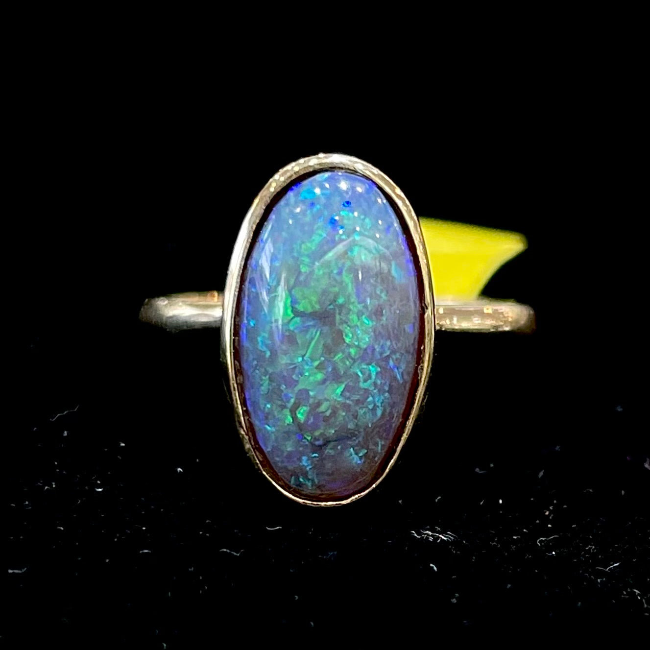 A simple yellow gold solitaire ring with a bezel set Lightning Ridge black crystal opal from Australia.
