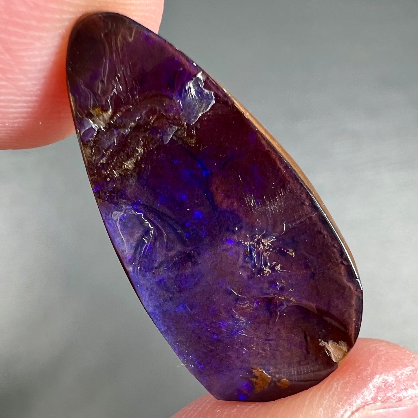A loose, teardrop shaped purple boulder opal stone.