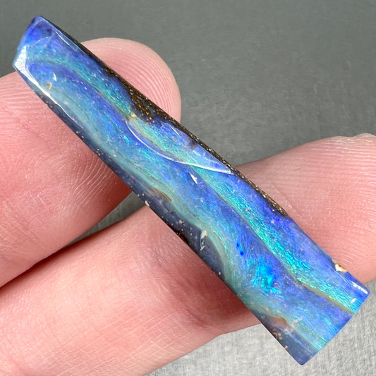 A loose, polished, wedge shaped boulder opal stone from Queensland, Australia.