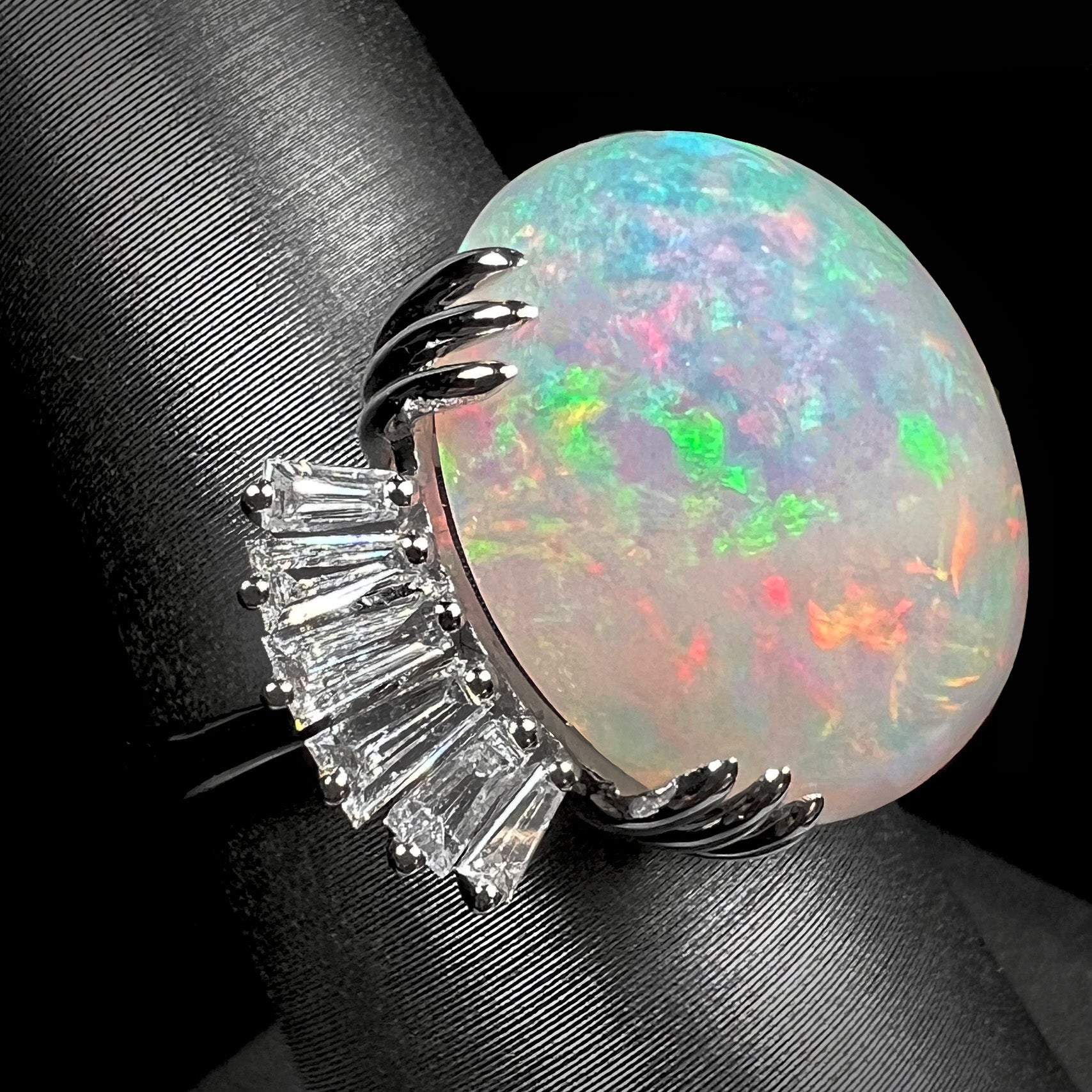 An oval cabochon cut opal mounted in a ladies' white gold ring between tapered baguette cut diamonds.