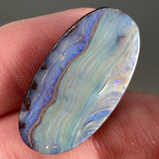 A loose, oval cabochon cut boulder opal stone from Queensland, Australia.