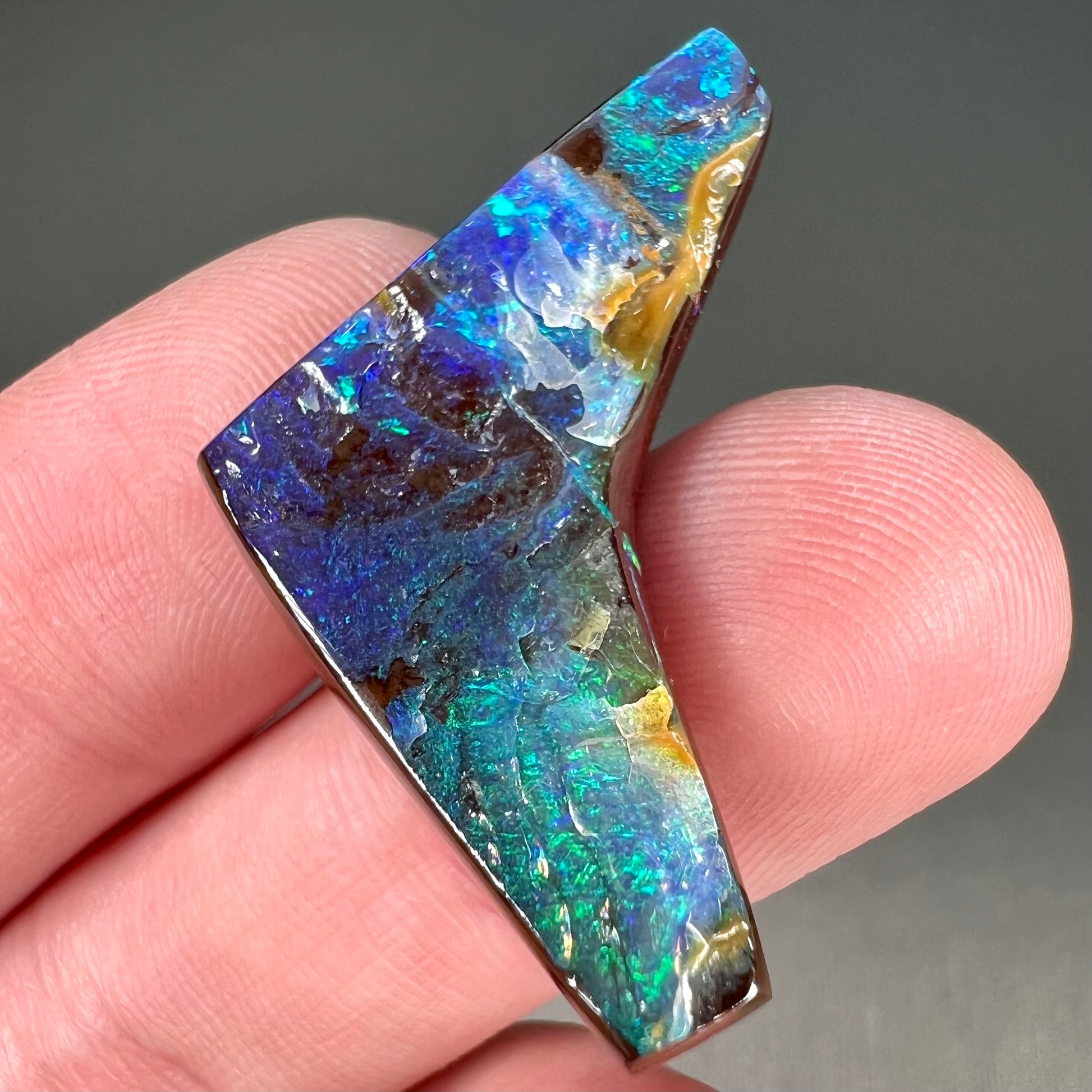 A loose, boomerang shaped boulder opal stone from Quilpie, Australia.  The stone is predominantly blue and green.