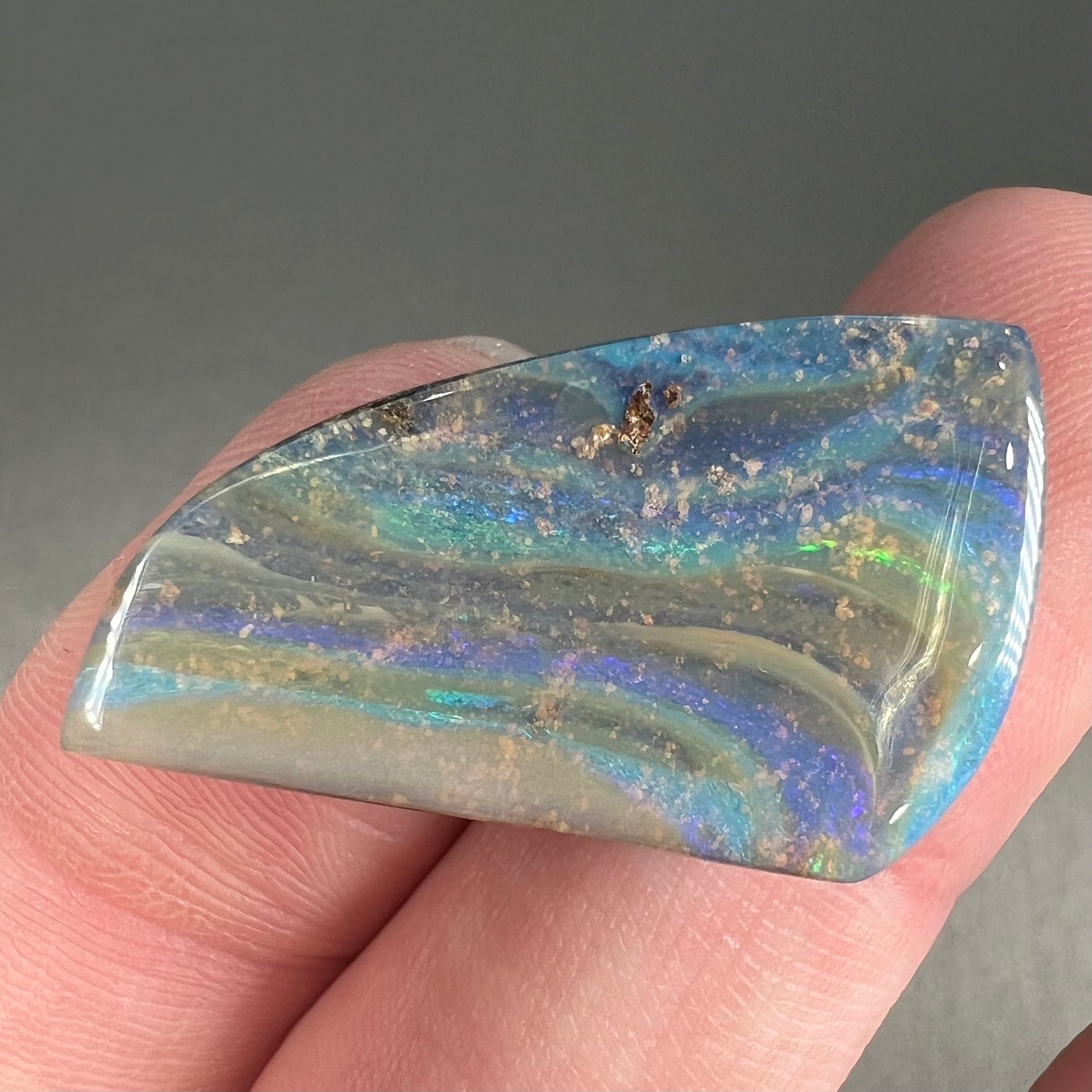 A polished, freeform shaped boulder opal stone from Queensland, Australia.  Predominant colors are green, blue, and violet.