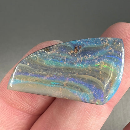 A polished, freeform shaped boulder opal stone from Queensland, Australia.  Predominant colors are green, blue, and violet.