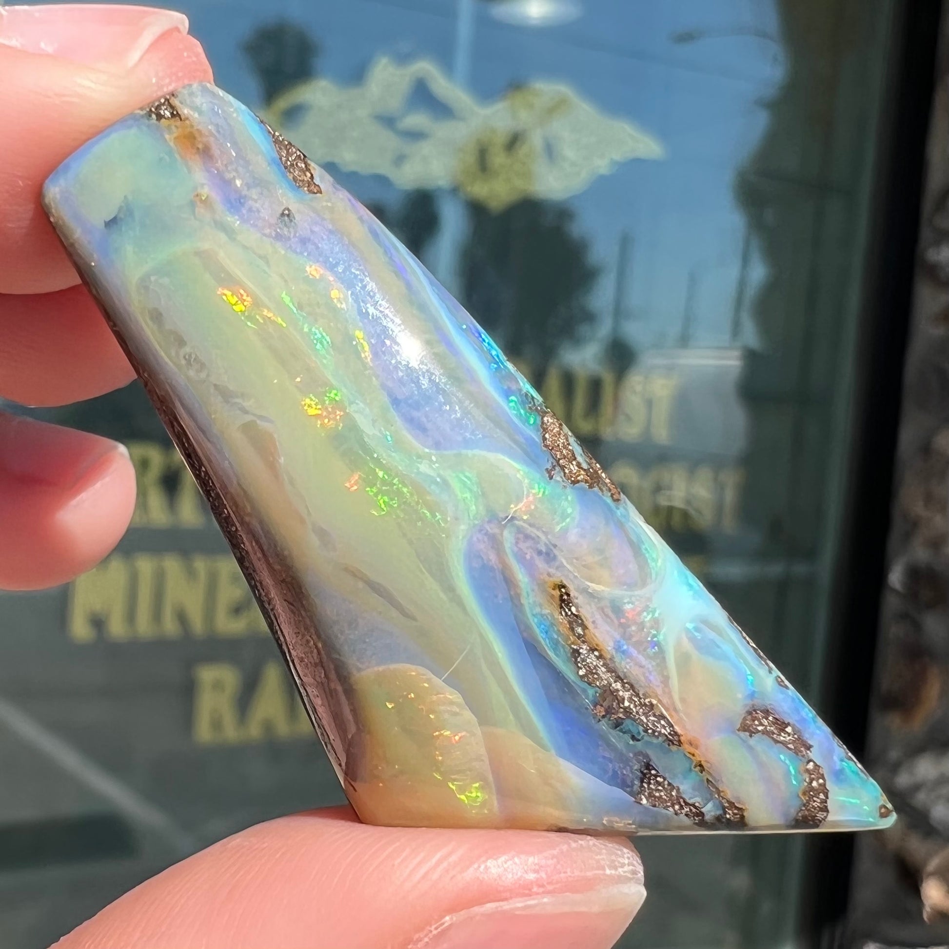 A freeform shaped, polished boulder opal stone from Queensland, Australia.  The stone has red, orange, green, and blue fire.