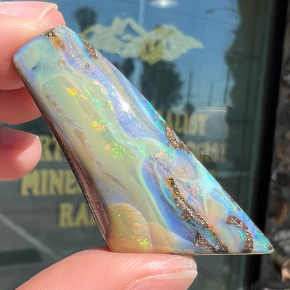 A freeform shaped, polished boulder opal stone from Queensland, Australia.  The stone has red, orange, green, and blue fire.