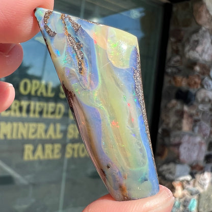 A freeform shaped, polished boulder opal stone from Queensland, Australia.  The stone has red, orange, green, and blue fire.