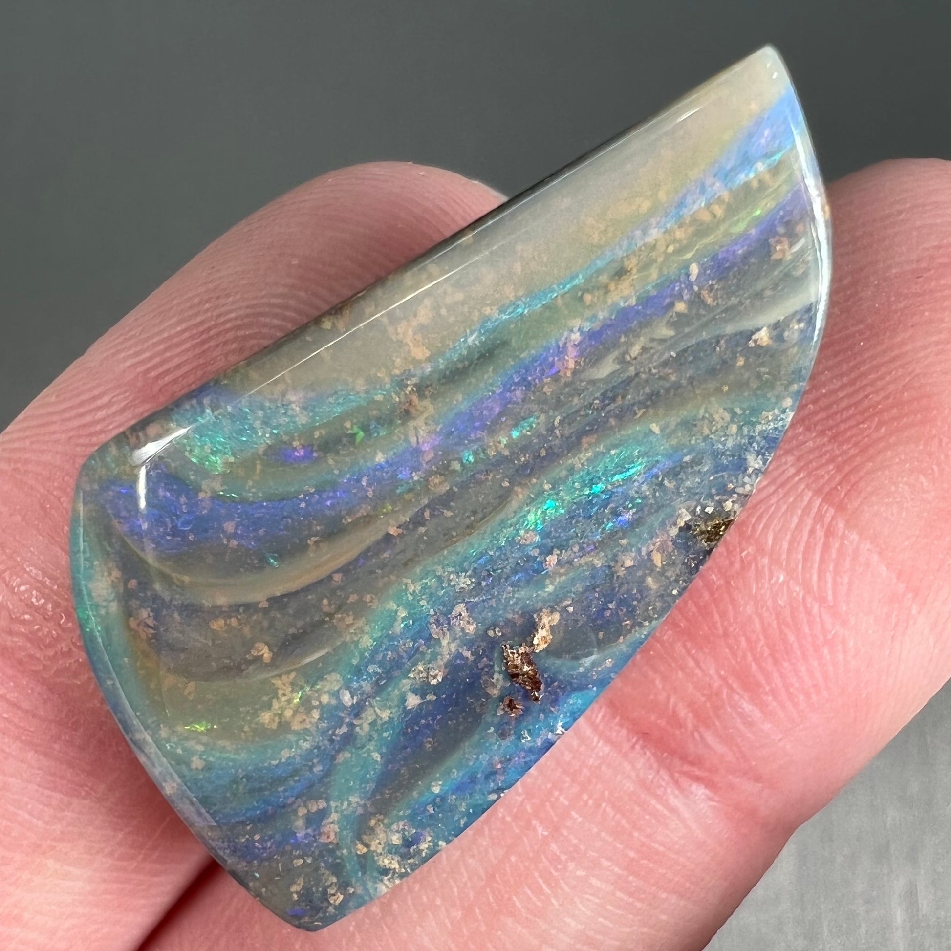A polished, freeform shaped boulder opal stone from Queensland, Australia.  Predominant colors are green, blue, and violet.