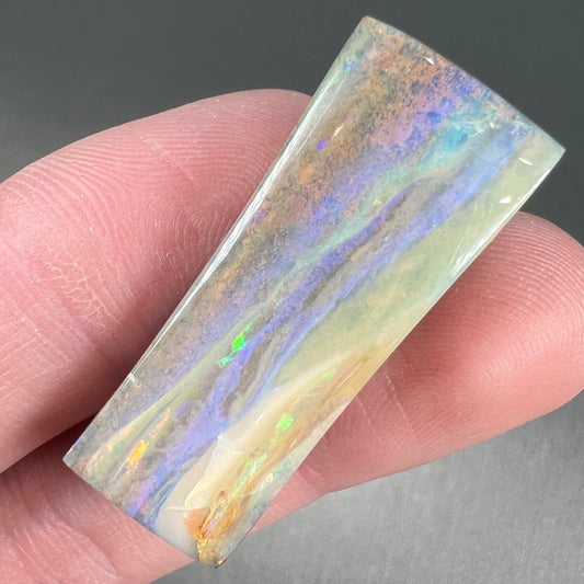 A polished, tapered rectangular cut boulder opal stone from Quilpie, Australia.