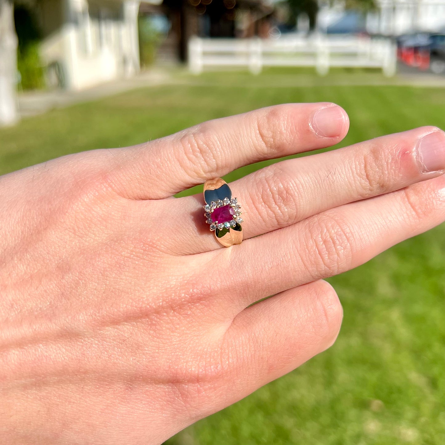 A yellow gold ring set with an emerald cut red ruby surrounded by a halo of round diamonds.