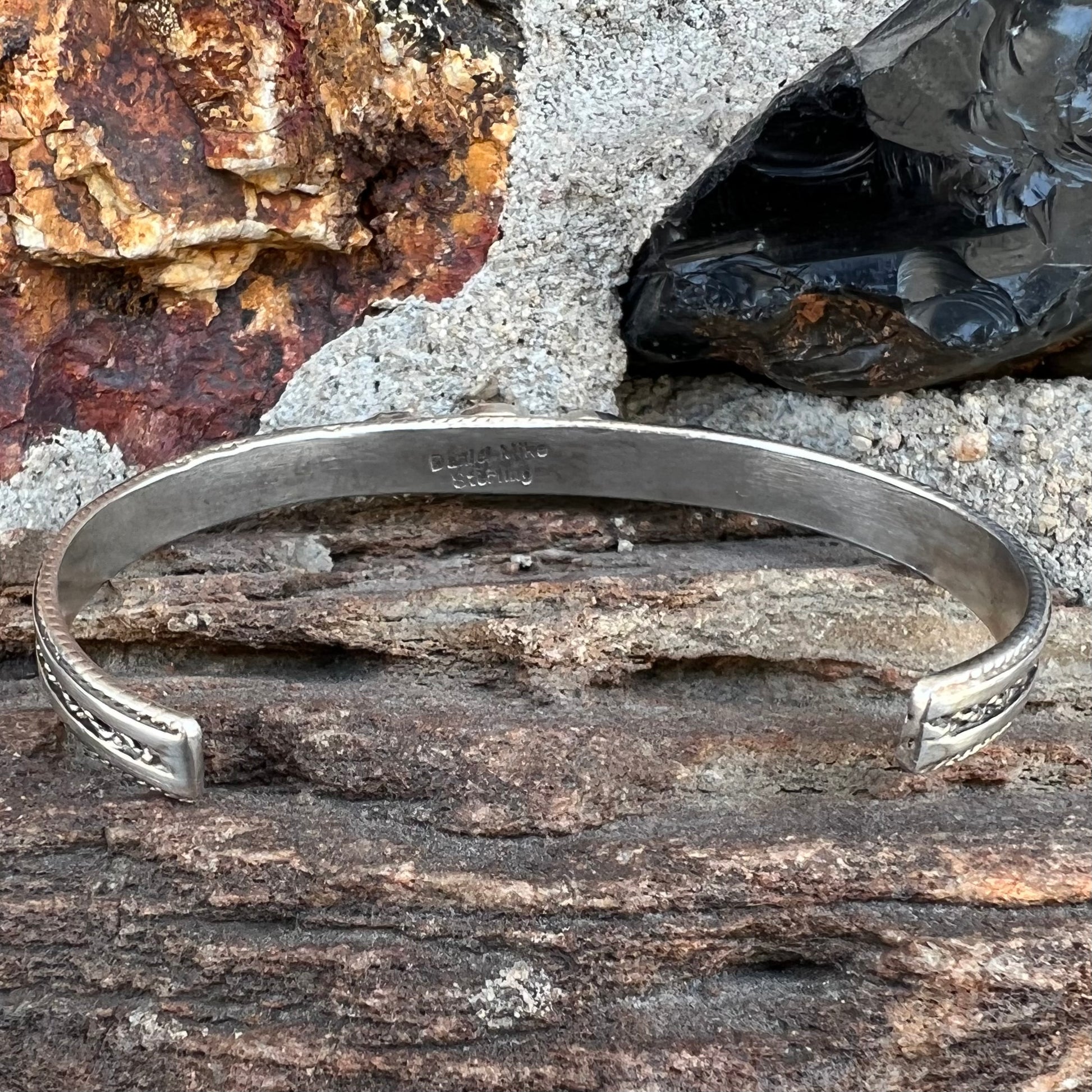 A silver rope cuff bracelet set with coral, turquoise, gaspeite, and lapis lazuli stones.  The underside is stamped "Daniel Mike".