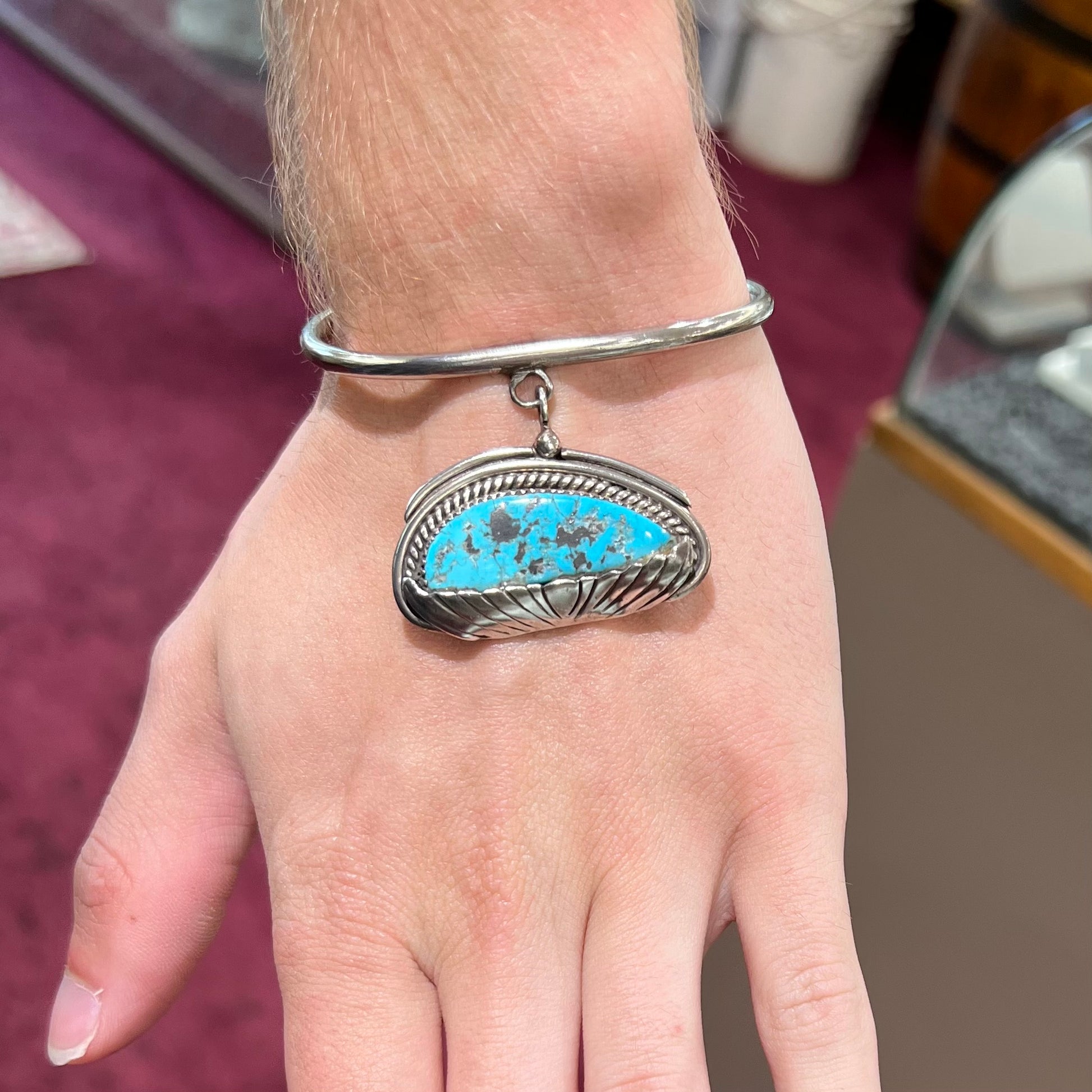 A sterling silver cuff bracelet with an attached dangle segment set with a turquoise stone from Pinto Valley.