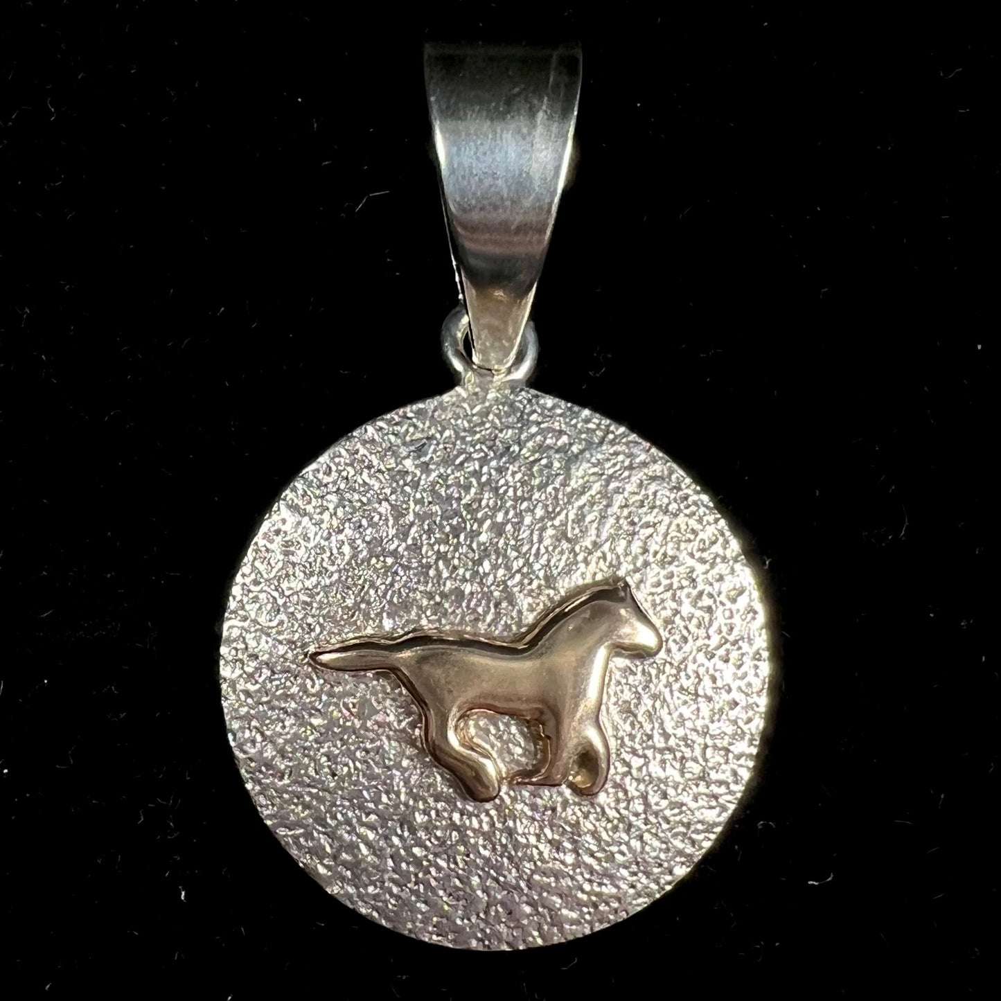 A Navajo-made sterling silver pendant depicting a yellow gold horse galloping.