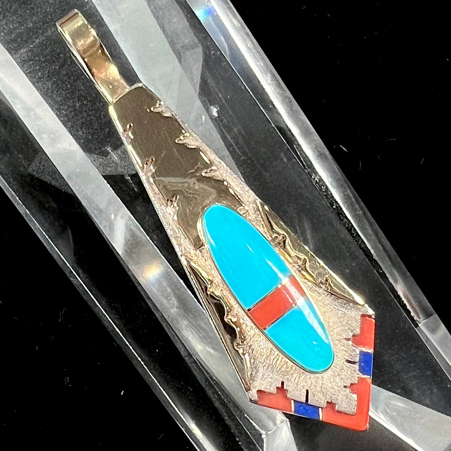 A yellow gold and sterling silver pendant inlaid with turquoise, coral, and lapis lazuli stones.  The piece is made by an unknown Native American artist and signed with the initials "LY".
